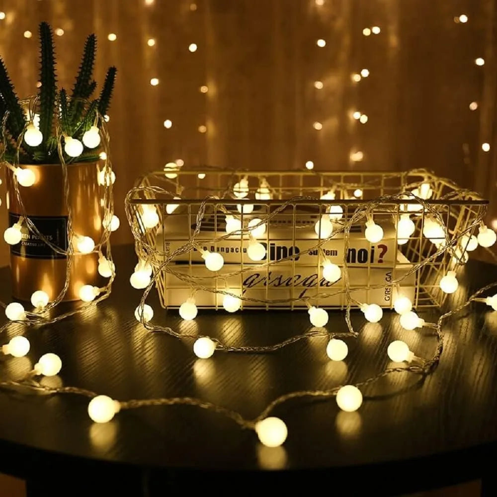 Warm white globe string lights glowing on a tabletop beside a plant and basket
