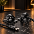 Black self-adhesive cable organizer clips on a dark desk with a cable secured in place